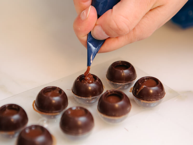 Close-up of hand piping ganache into chocolate